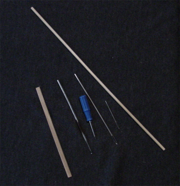 Several small tools on a dark background, including 2wood dowels, 2 tapestry needles of different sizes, a small awl and a tiny crochet hook.